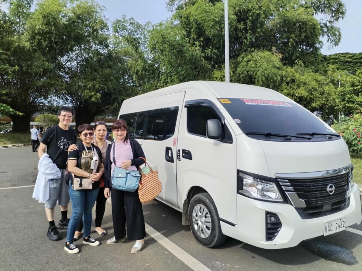 Happy Japanese family of 6 standing next to their premium Hyundai Staria van after airport pickup service